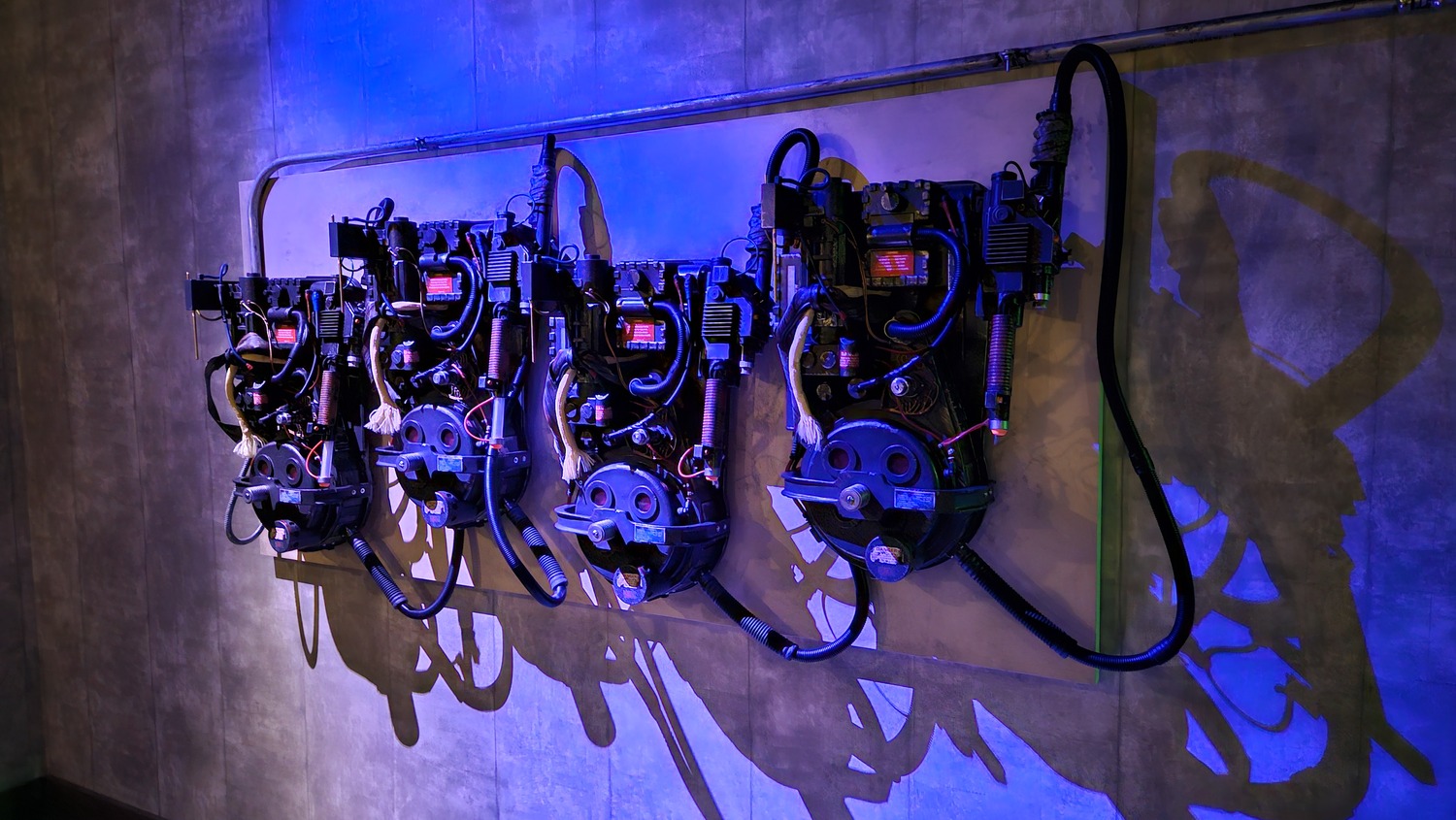 Four proton packs are displayed on a wall, illuminated by blue lighting.