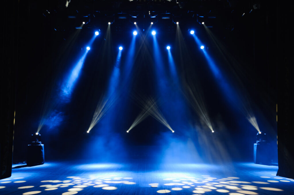 Stage illuminated with multiple blue spotlights, casting beams and patterns on the floor, shrouded in light mist.