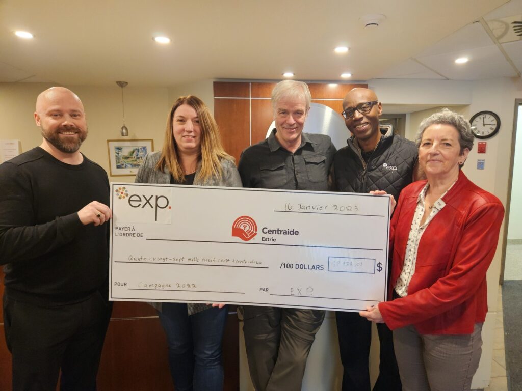 Five people stand indoors holding a large novelty check from exp. for Centraide Est-Quebec, dated January 2023, with an amount of $27,989.41.