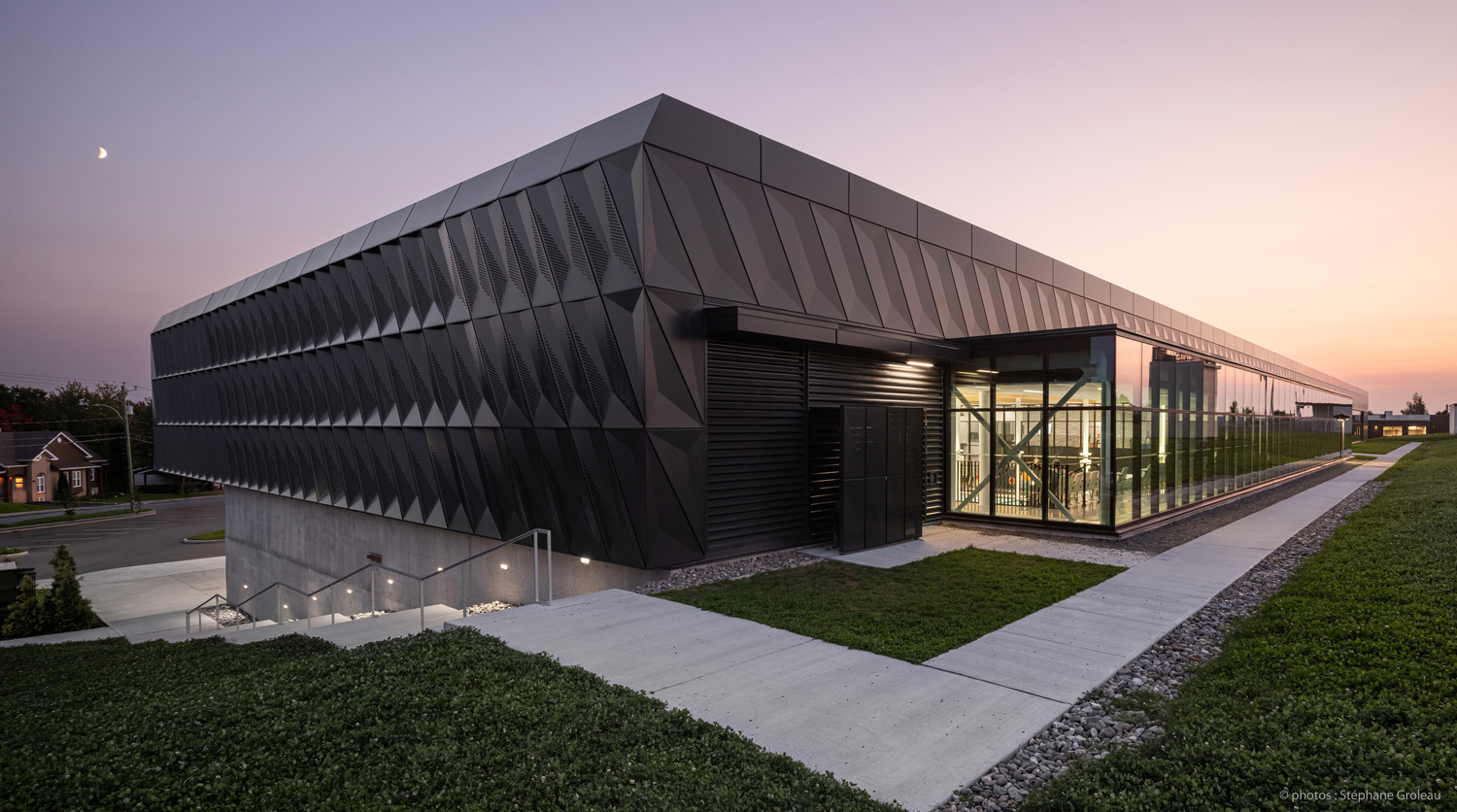 Modern office building at dusk featuring a sleek, angular design with expansive glass windows and subtle outdoor lighting, under a twilight sky with a visible crescent moon.