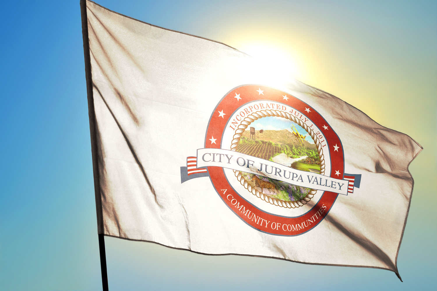 Flag of Jurupa Valley waving in the sunlight, featuring the city's seal with a landscape and text.