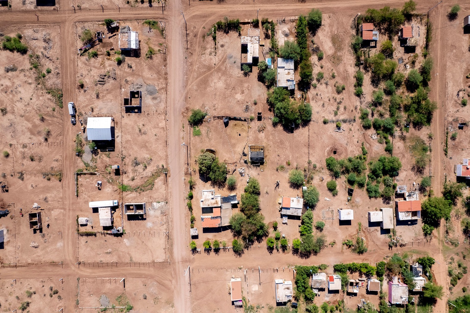 Aerial view of a rural area with scattered houses, dirt roads, and patches of vegetation. The settlements are dispersed across a roughly grid-like pattern.