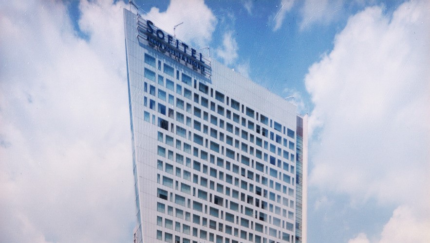 A tall, modern hotel building with the signage "Sofitel" on the roof, set against a partly cloudy sky.