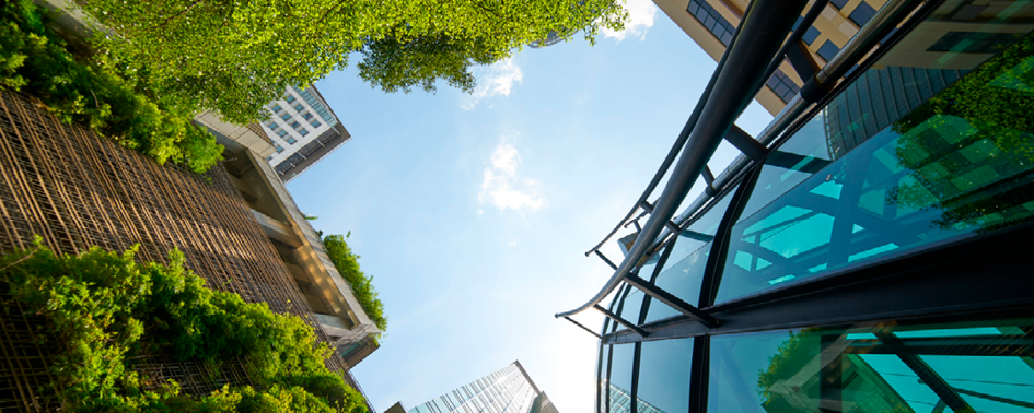 Looking up at modern buildings with greenery and blue glass structures against a clear sky.
