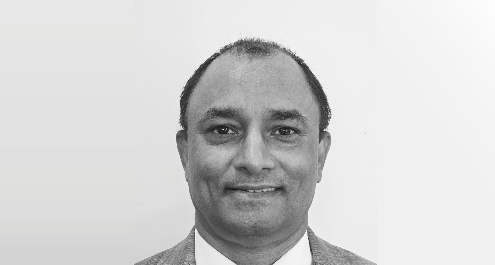 A black-and-white photo of a man in a suit and tie, smiling, with a plain background.