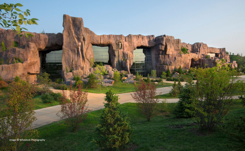 A building with a facade designed to look like a rocky cliff, featuring large glass windows and surrounded by landscaped greenery and pathways.