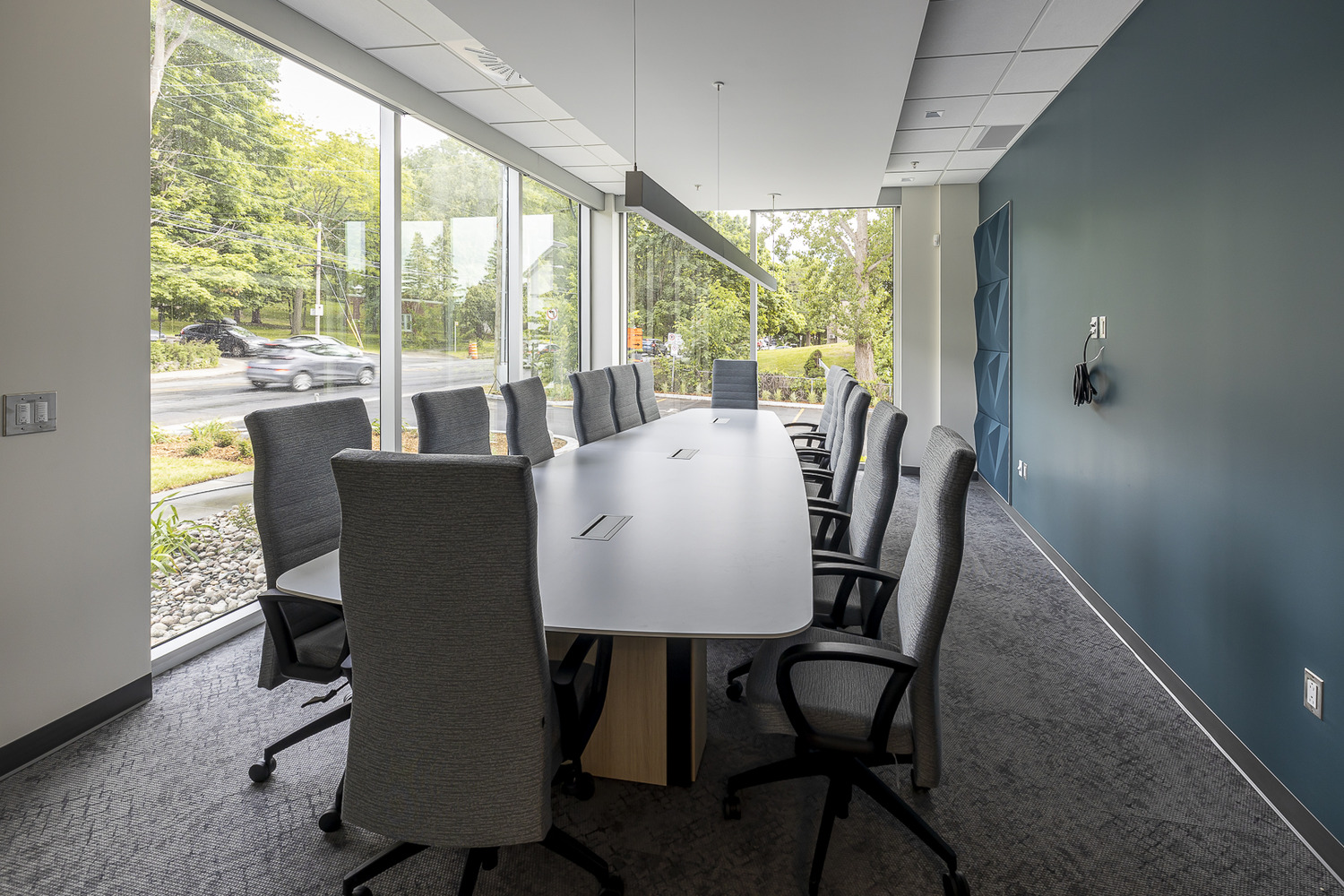 Conference room with a long table, surrounded by tall gray office chairs, large windows on one side, and a blue accent wall.