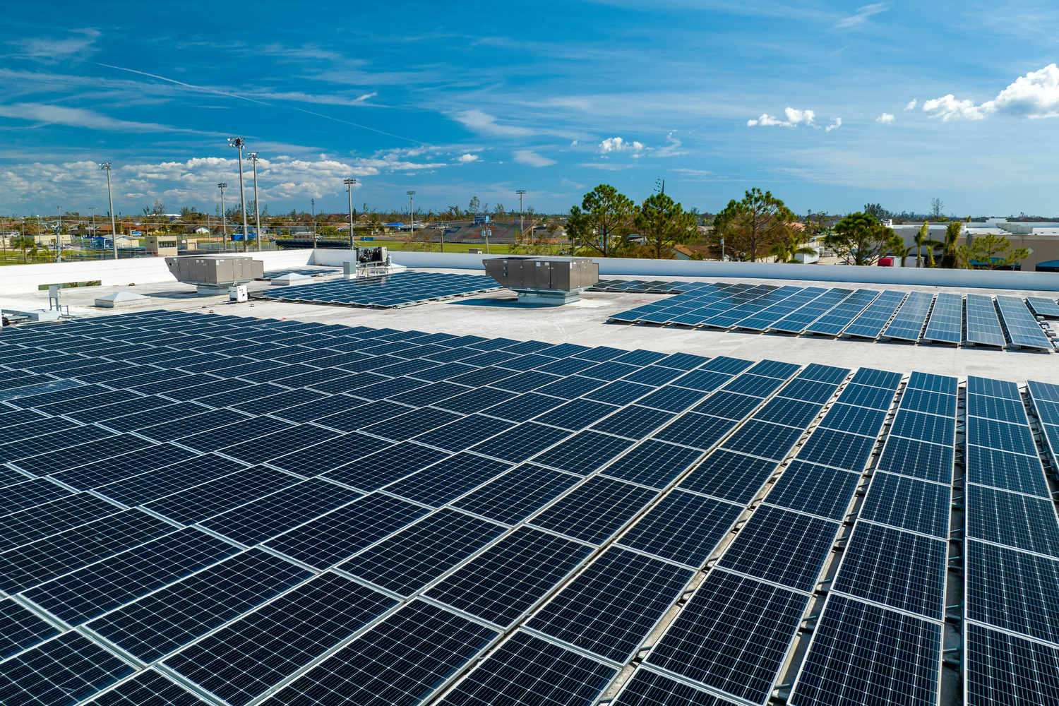 Rooftop solar panels under a clear blue sky with buildings and trees in the distant background.