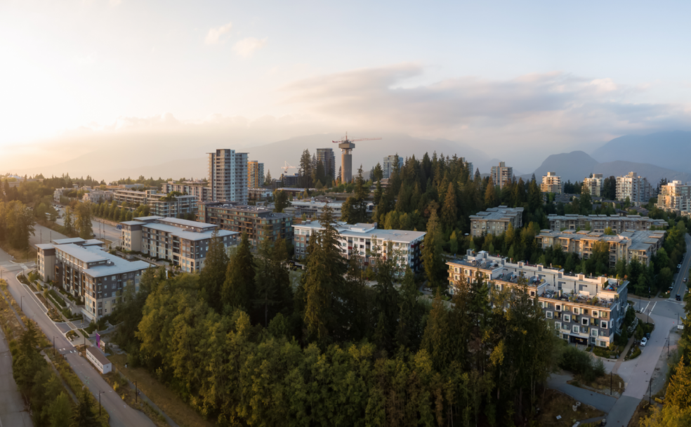 Aerial view of a residential area with multiple mid-rise buildings surrounded by trees and mountains in the background. A construction crane is visible in the center of the image.