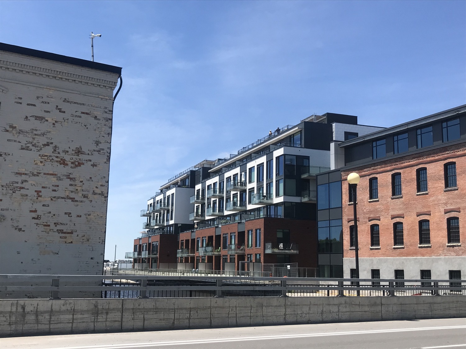 Modern apartment buildings with glass balconies next to an older brick structure under a clear blue sky.