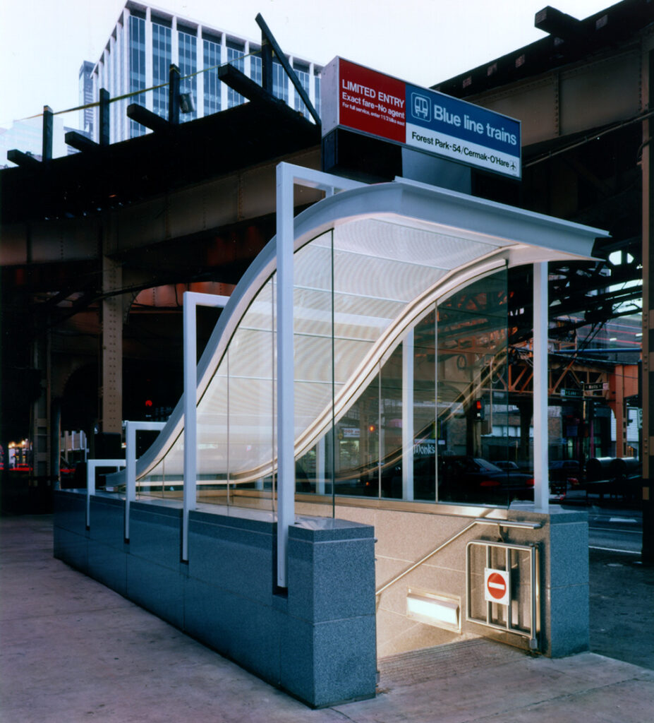 Entrance to a modern subway station with a wavy glass canopy, stairs descending underground, and a sign for Blue Line trains in the background.