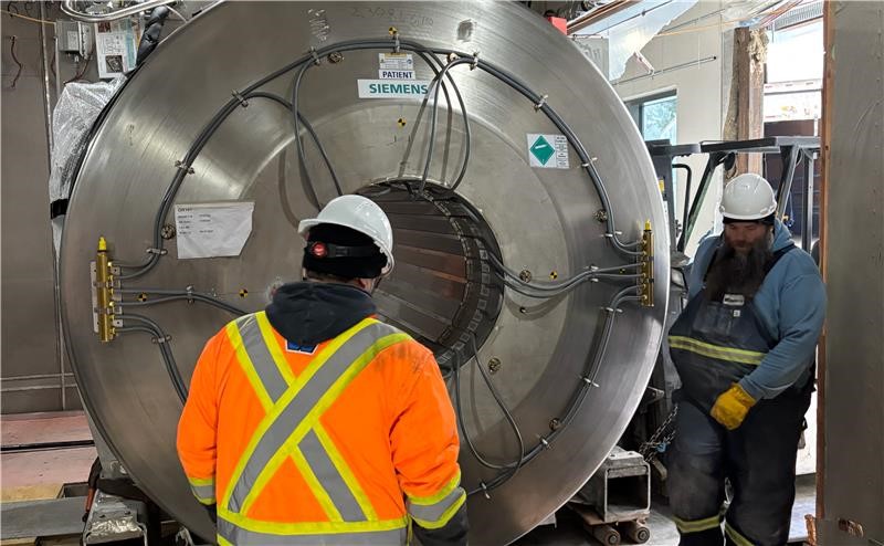 Workers in safety gear examine industrial machinery in a warehouse setting.