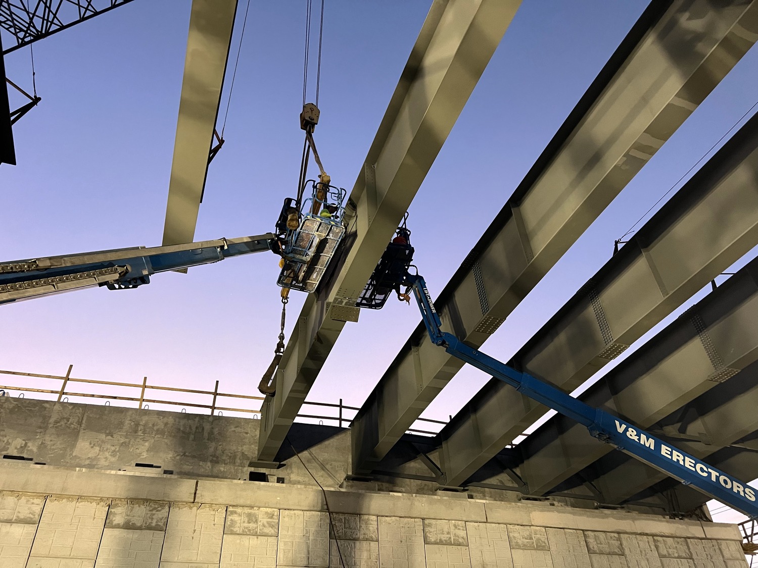 Construction workers on lifts install steel beams on a bridge under construction.