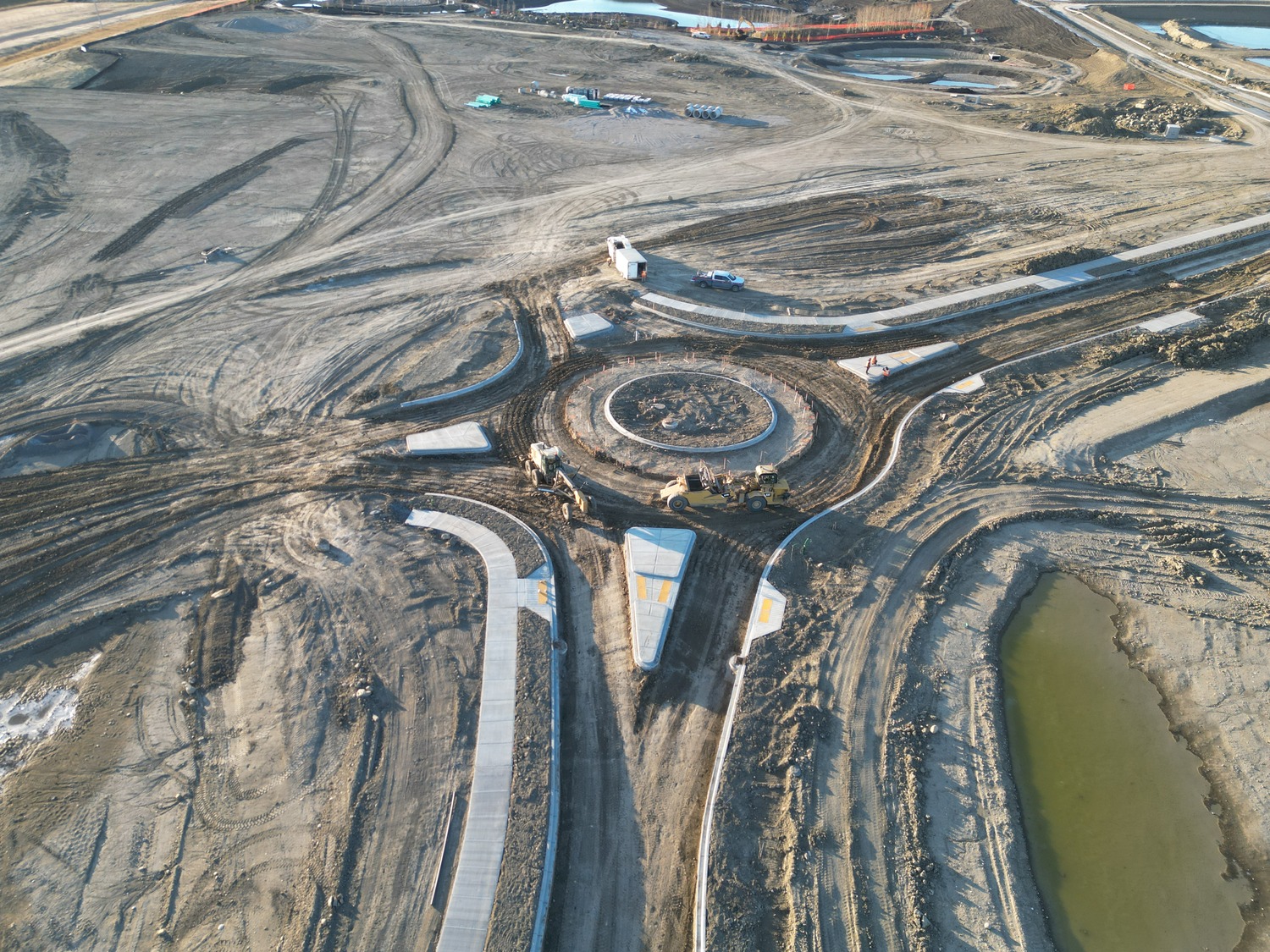 Aerial view of a road construction site featuring a roundabout in progress. Surrounding areas are mostly dirt and machinery is present.