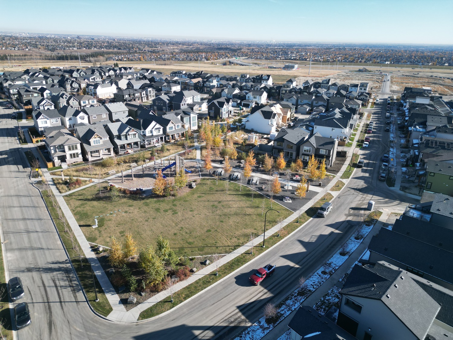 Aerial view of a suburban neighborhood with rows of houses, a central grassy park with a playground, and surrounding roads.