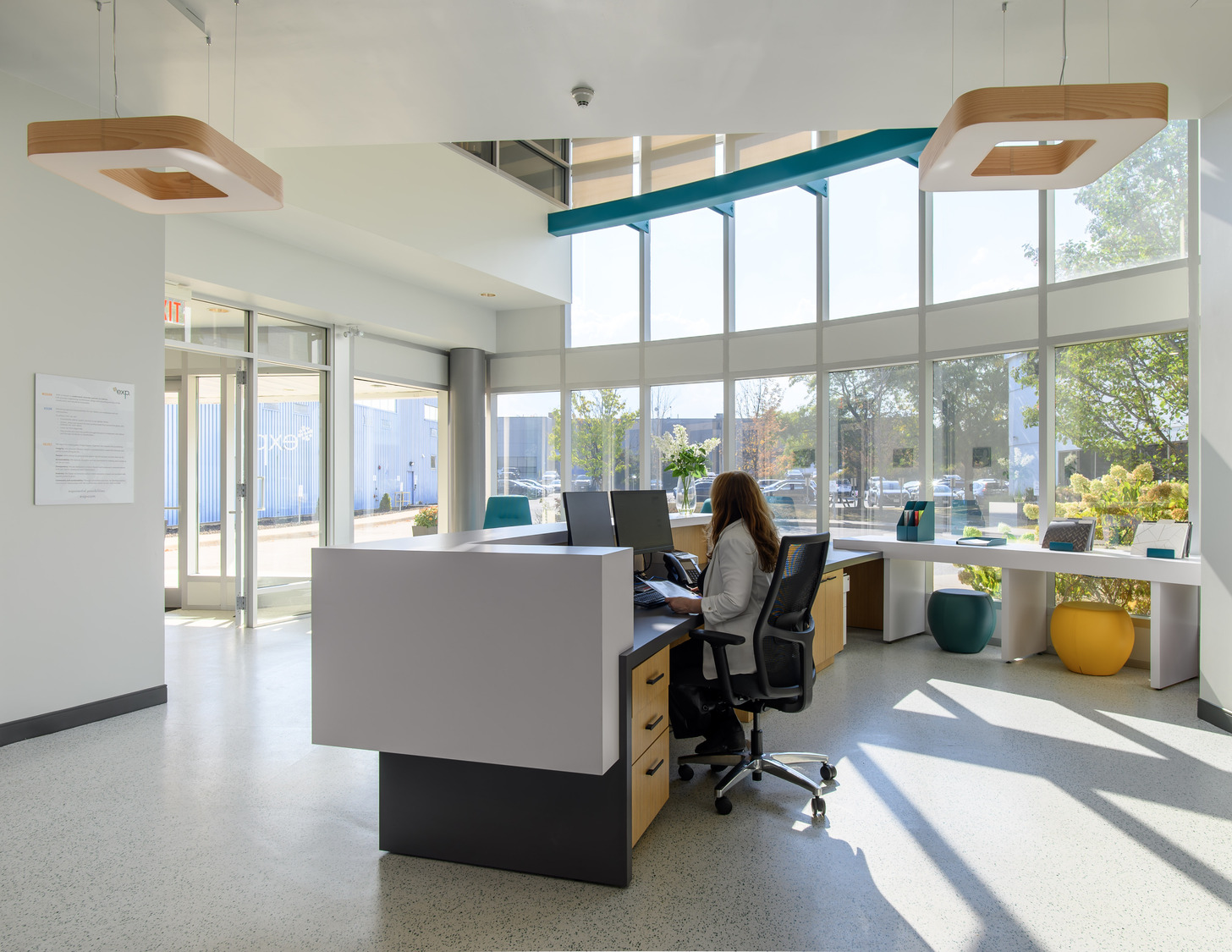 A person seated at a desk in a brightly lit modern office, with large windows and contemporary furniture.