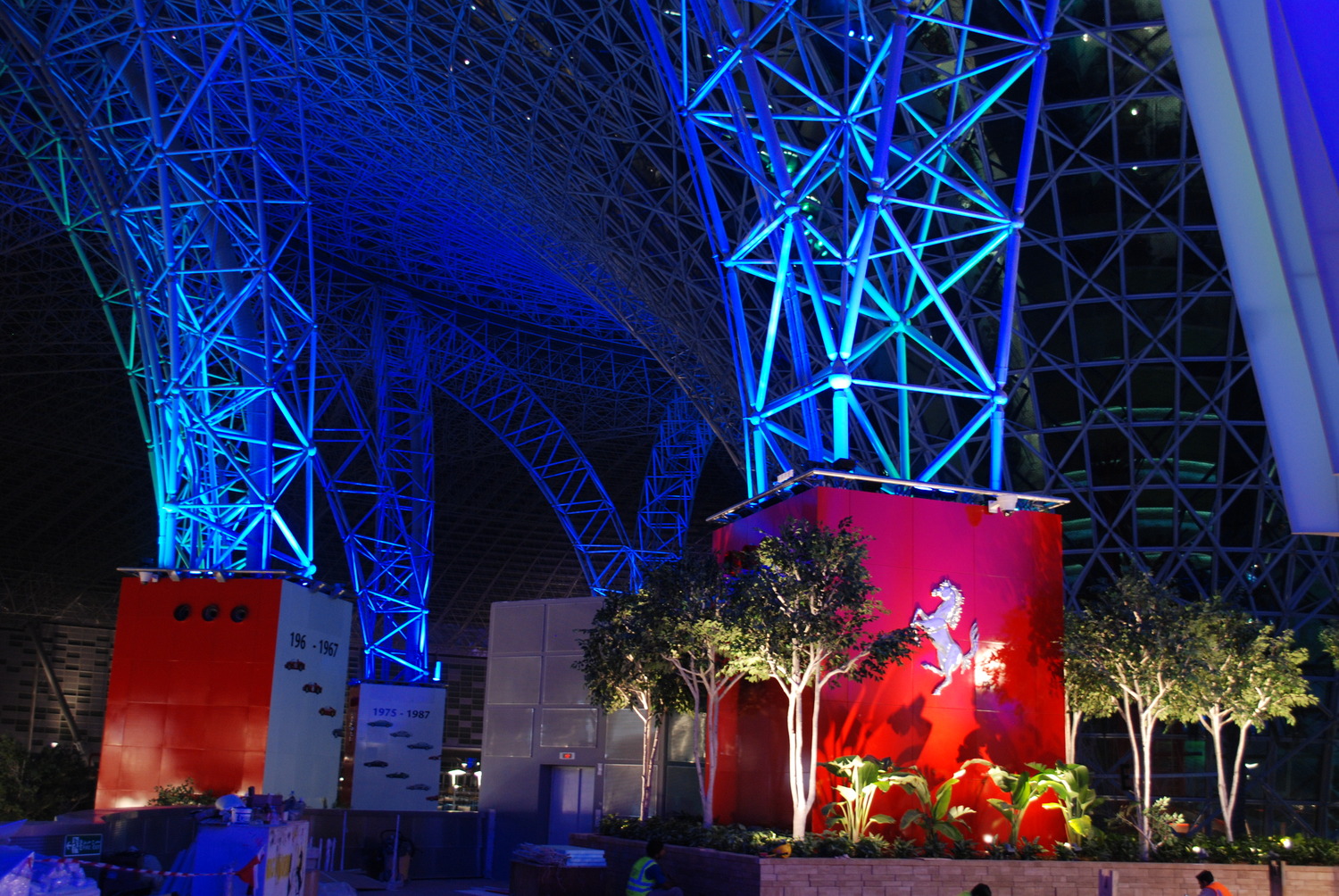 Blue and red illuminated structure with trees and a horse emblem, featuring intricate geometric metal framework.