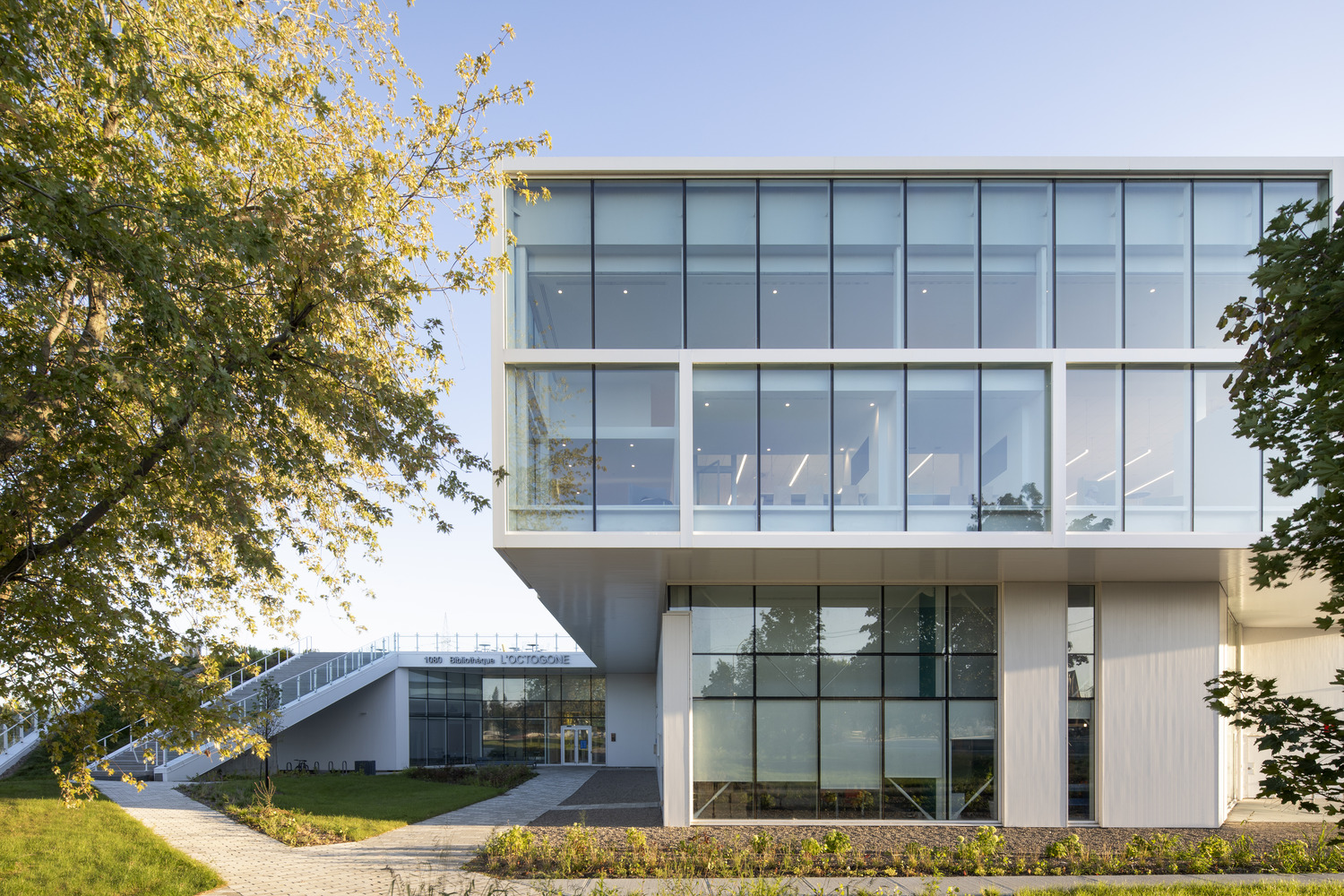 Modern building with large glass windows, surrounded by trees and greenery, under a clear blue sky.