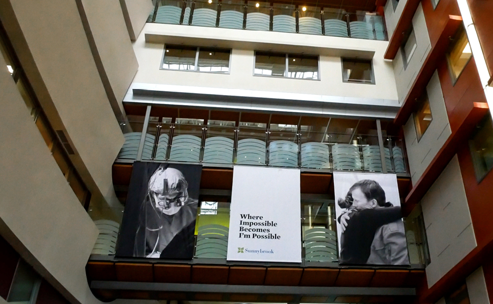 Interior view of an atrium with large banners hanging. Central banner reads, "Where Impossible Becomes I'm Possible," flanked by black-and-white images of people in various activities.