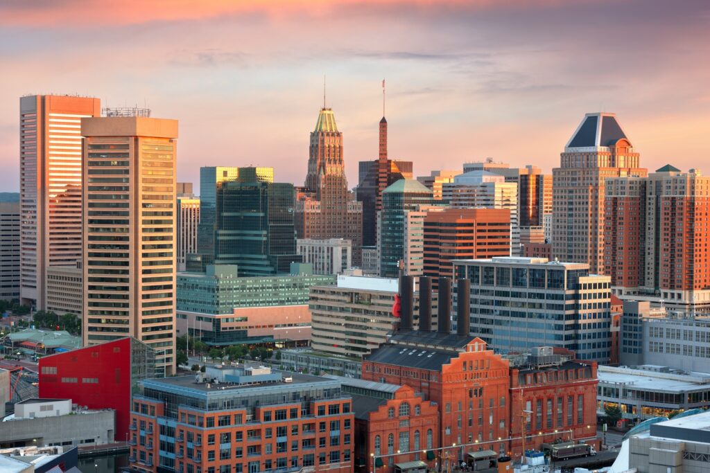 The skyline of a city at sunset presents a blend of modern and historic buildings, where towering skyscrapers meet classic red brick architecture. As preparations for SASHTO 2025 unfold, enhanced transportation links add to the city's vibrant and dynamic allure.