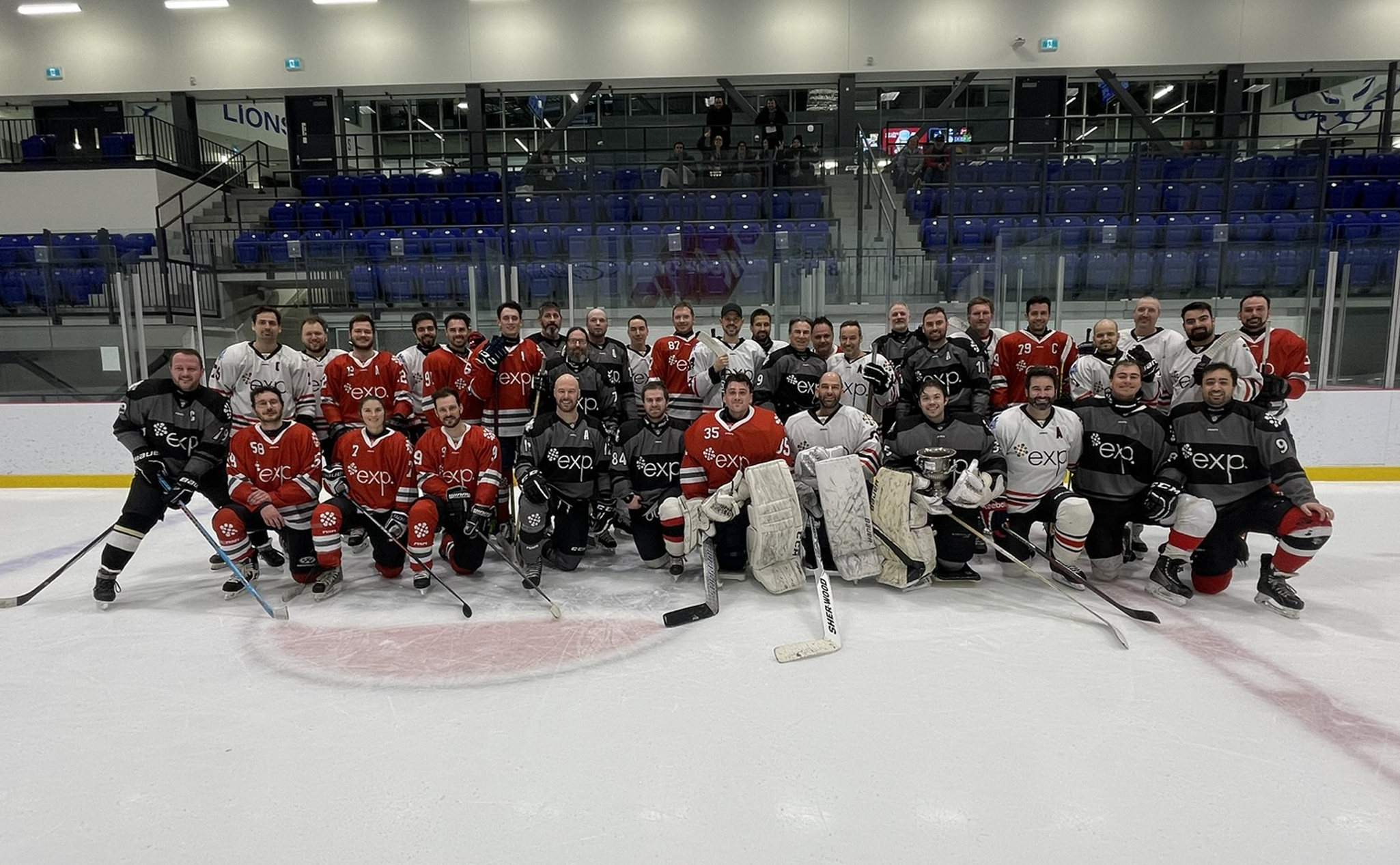 Une photo de groupe de joueurs de hockey sur la glace, portant des maillots noirs et rouges, avec de l'équipement et des bâtons de hockey, dans une patinoire intérieure.