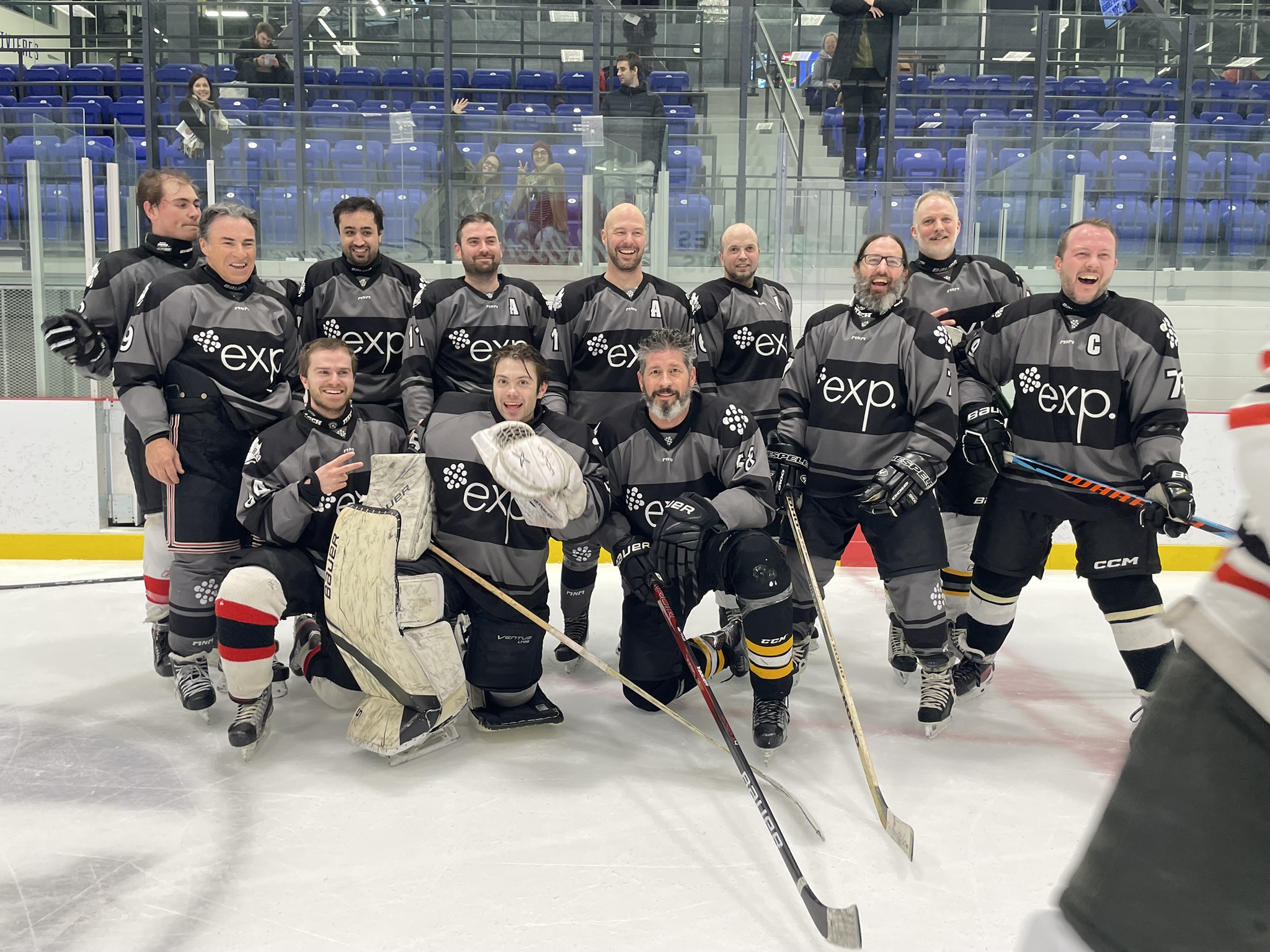 Une équipe de hockey en maillot noir pose sur la patinoire. Les joueurs sourient et sont debout ou à genoux pour une photo de groupe.