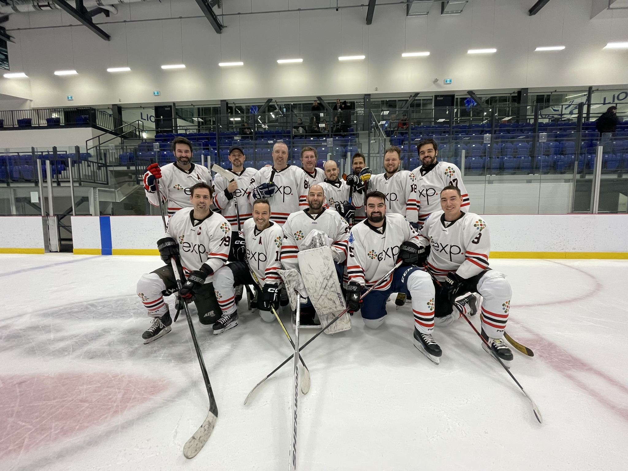 Une équipe de hockey en maillot blanc pose sur la glace d'une patinoire, avec des joueurs tenant des bâtons et portant des patins et des casques.