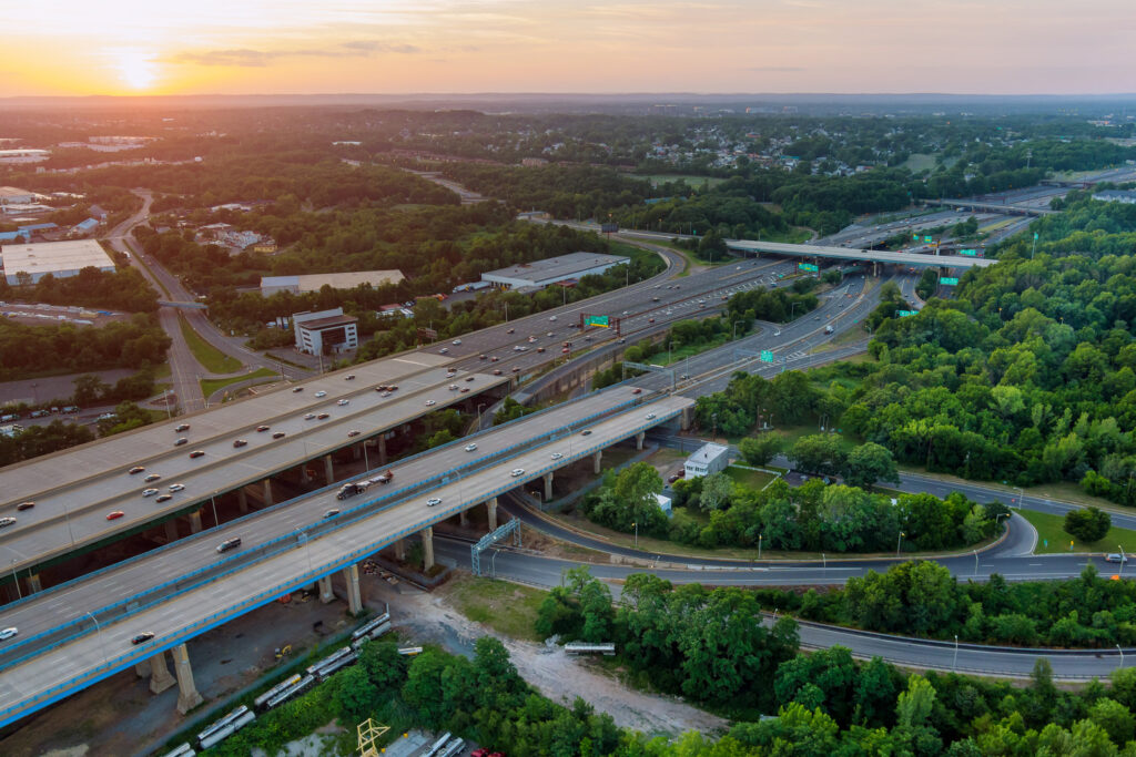 An aerial view of the highway interchange at sunset captures the essence of transportation's future. Surrounded by greenery and buildings, multiple roads and overpasses weave together in a ballet of motion, reflecting the vision for NASTO 2025.