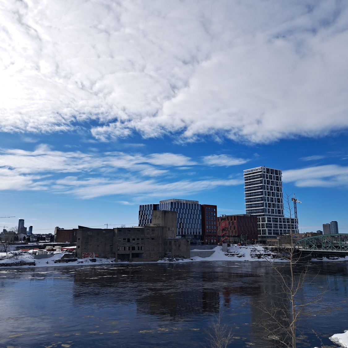 Skyline with modern buildings in ZIBI Waterfront City by a river, scattered snow on the ground, and a partly cloudy sky above.